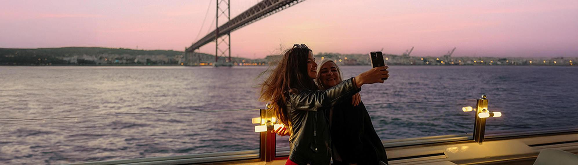 Crucero al atardecer en Portugal por FRS: dos mujeres se toman un selfie frente al puente 25 de abril