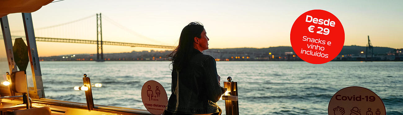 A woman standing on the deck of the boat and watching the sunset at the Tagus.