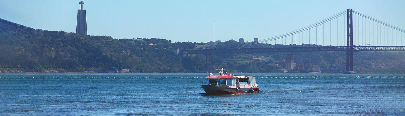 Ship on the Tagus River with blue sky and Cristo Rei and the bridge 25 de Abril in the background.
