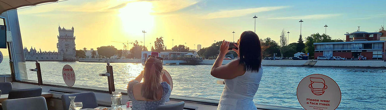 Two women on the vessel taking pictures of the Tower of Belém passing by.