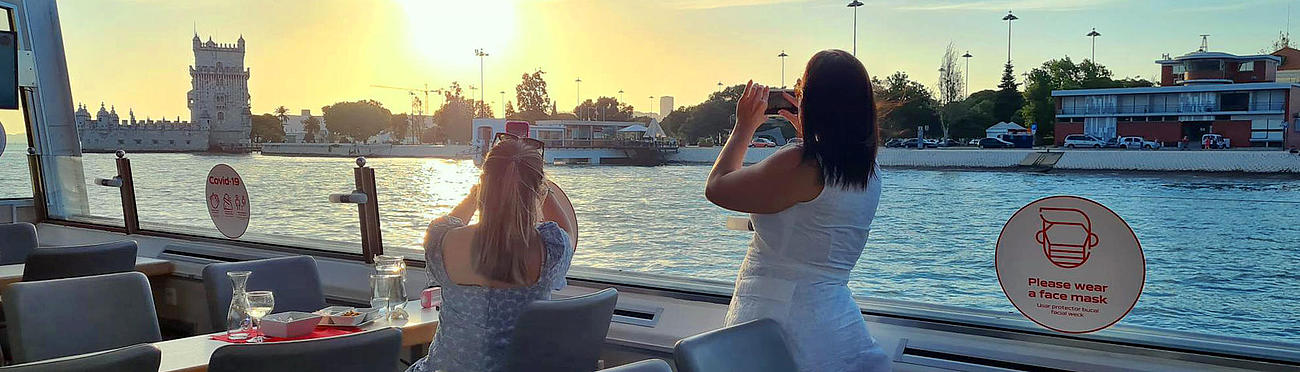 Two women on the vessel taking pictures of the Tower of Belém passing by.