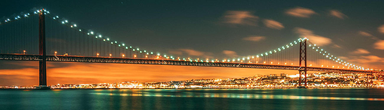 Die Brücke des 25. April und die abendlich beleuchtete Promenade von Lissabon.