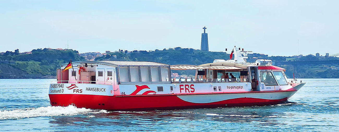 Barco navegando por el río Tajo, con Cristo Rey y el Puente 25 de Abril al fondo.