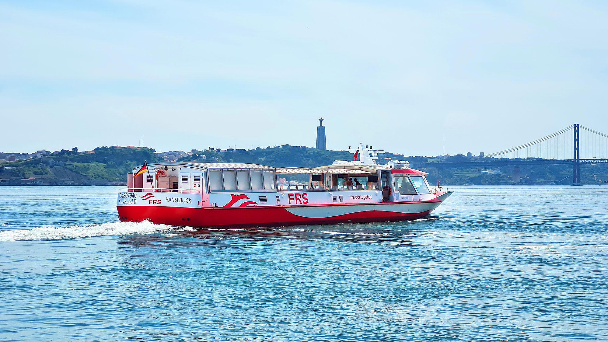 Vessel cruising on the Tagus river, Cristo Rei and the Ponte 25 de Abril in the background.