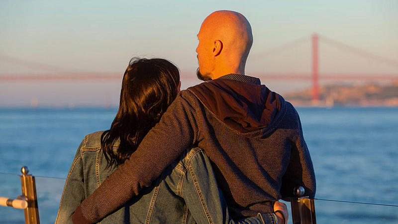 Ein Paar steht Arm in Arm auf dem Boot und beobachtet den Sonnenuntergang.