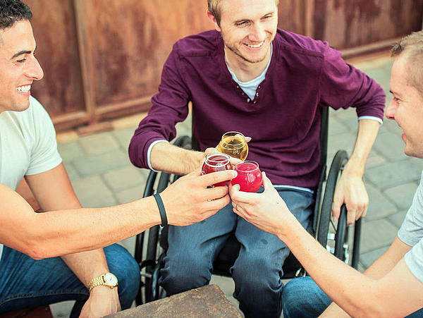 Three men toasting, one of them sitting in a wheelchair.