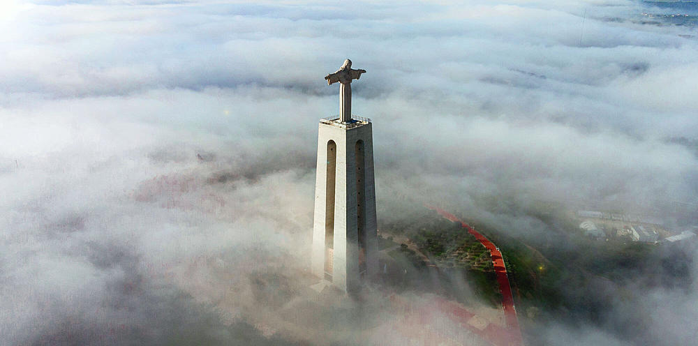 Die Christus-Statue "Santuário do Cristo Rei" in Almada, nebelverhangener Blick aus den Wolken.