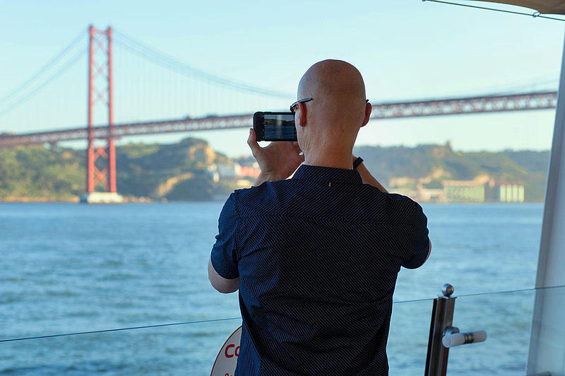 A man taking a picture of the bridge 25 de Abril from the vessel.